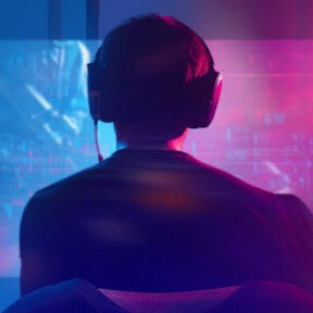 Mann sitzt vor Computer mit blauen und rosa Lichtern und ist am gamen